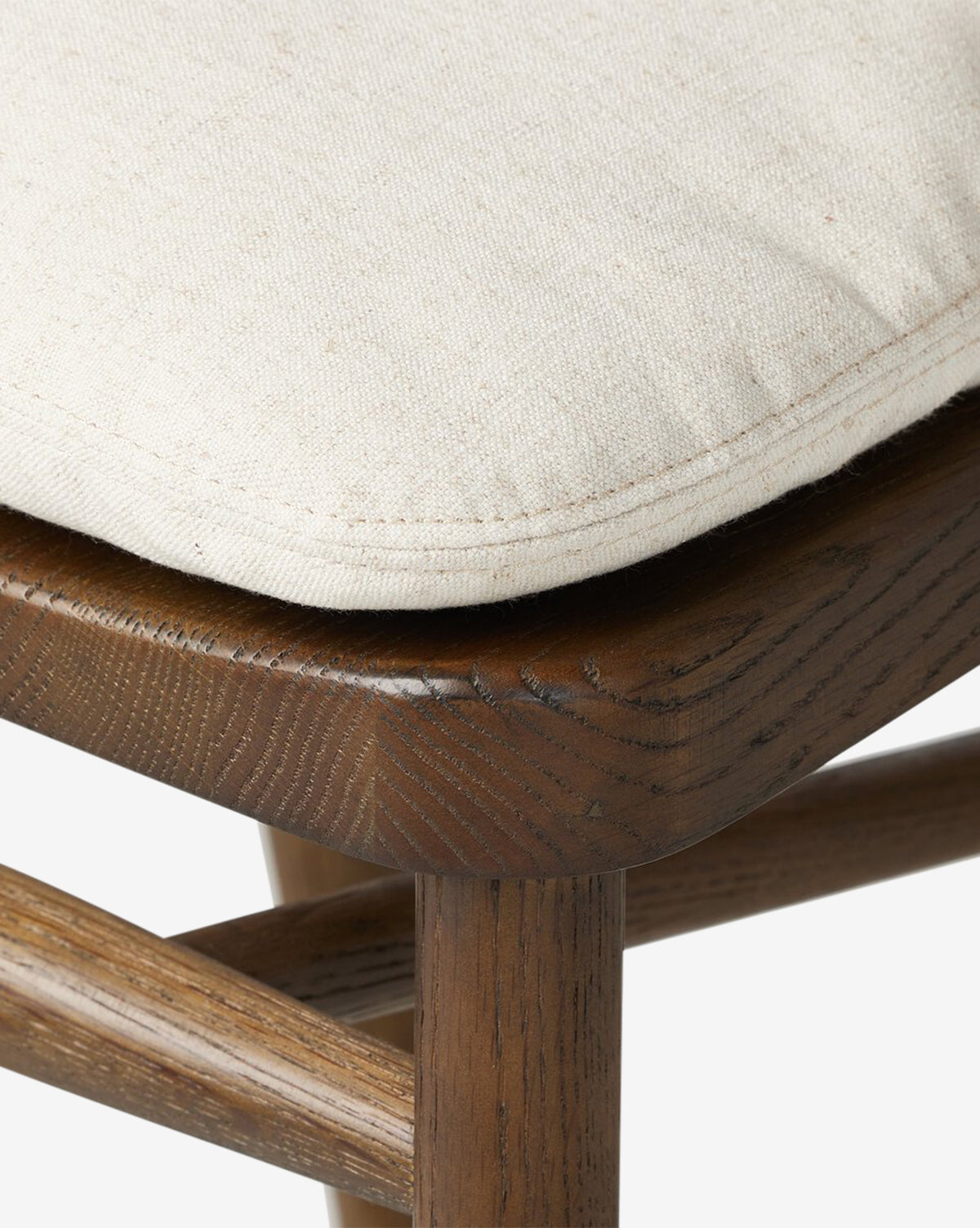 Close-up of the Ardent Stool by Four Hands, showcasing its solid oak frame with visible grain and subtle scratches. The beige upholstered cushion looks soft and textured—an ideal addition to any kitchen bar. Vendixs