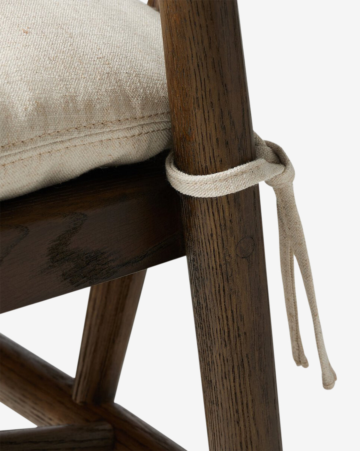 Close-up of the Four Hands Ardent Stool, featuring a solid oak frame with a dark finish and a light, textured cushion tied to the chair back—perfect for bringing comfort and style to any kitchen bar. Vendixs