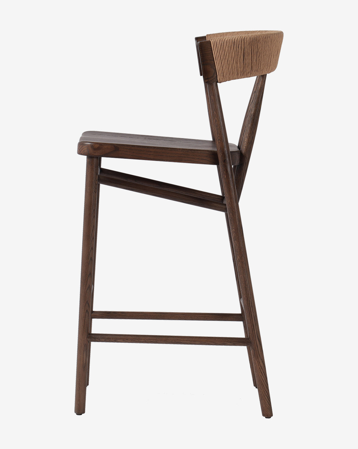 Side view of the Ardent Stool by Four Hands: a modern oak frame kitchen bar stool with a dark finish, flat seat, angled backrest with natural paper rush weave, and footrests connecting the legs. Vendixs