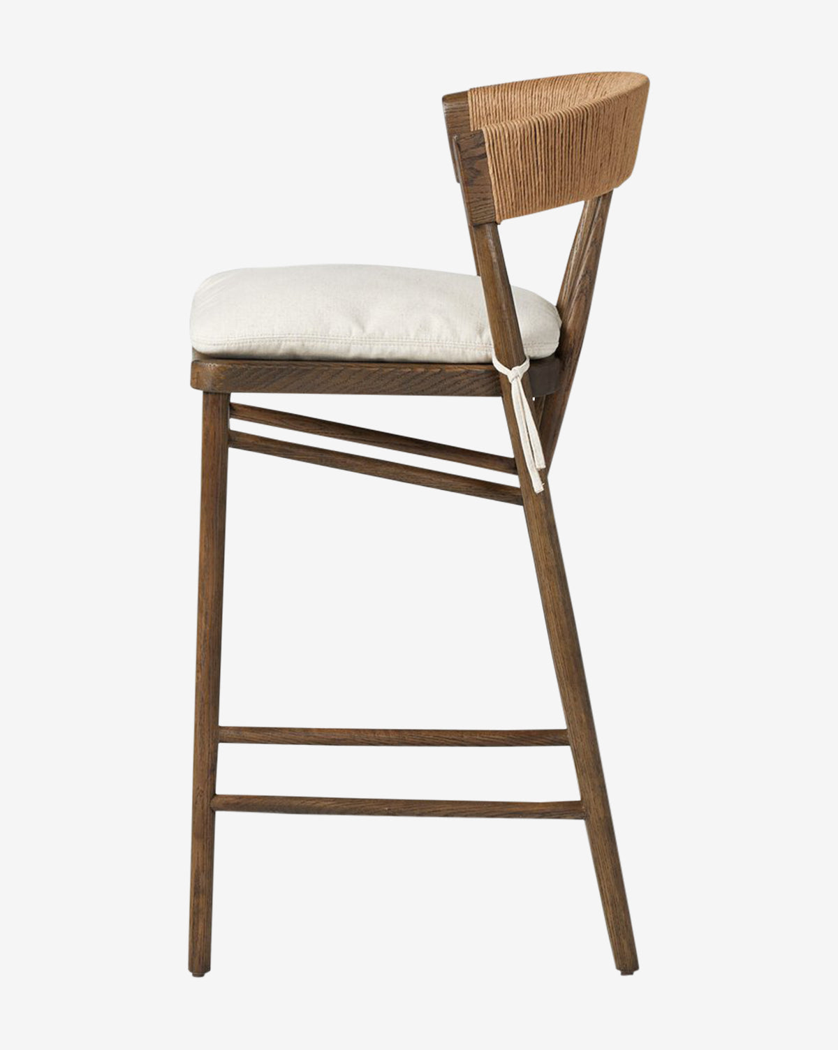 Side view of the Ardent Stool by Four Hands, featuring an oak frame, light cushioned seat, and woven paper rush backrest. Angled legs with horizontal supports offer a modern, minimalist look. Vendixs