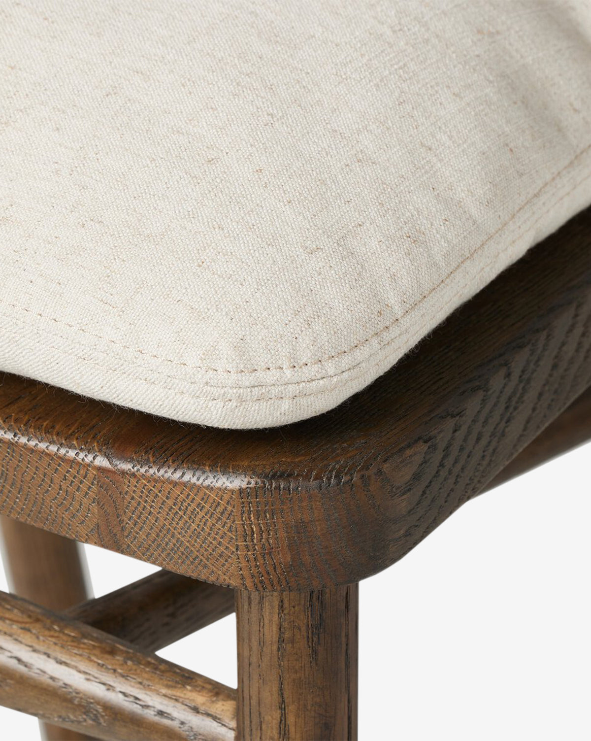 The Ardent Stool by Four Hands features a solid oak frame, dark wood grain, and a light beige textured cushion with detailed stitching—adding refined charm to any kitchen bar. Vendixs