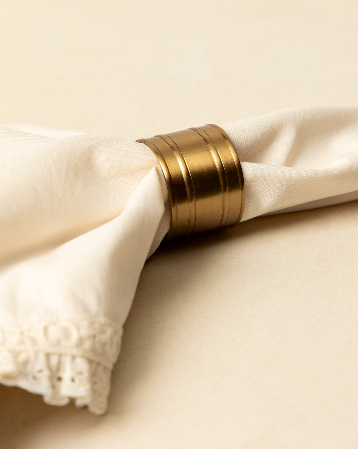 A cream-colored cloth napkin with lace trim is folded and secured by an Argent Napkin Ring, set on a light beige surface—an ideal touch to elevate your holiday table, by Vendixs