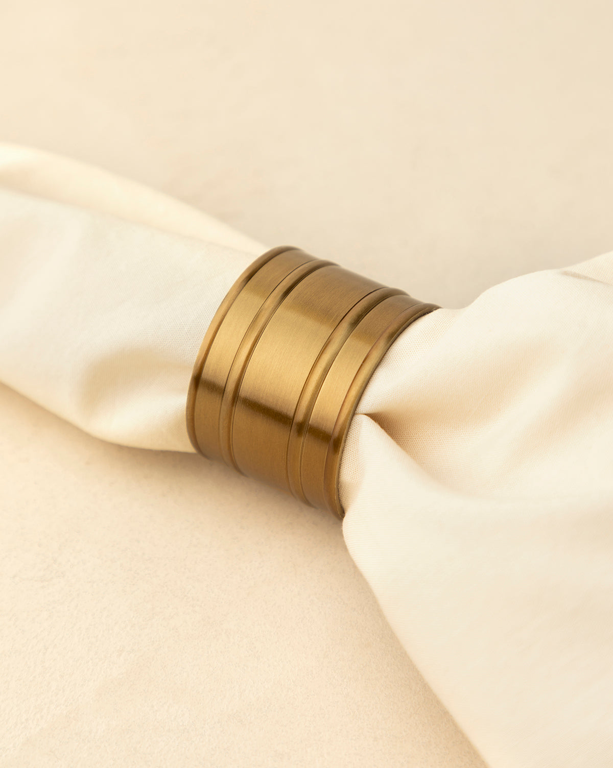 A close-up of an Argent Napkin Rings (Set of 4) holding a cream-colored napkin against a beige background—an elegant accent for your holiday table, by Vendixs