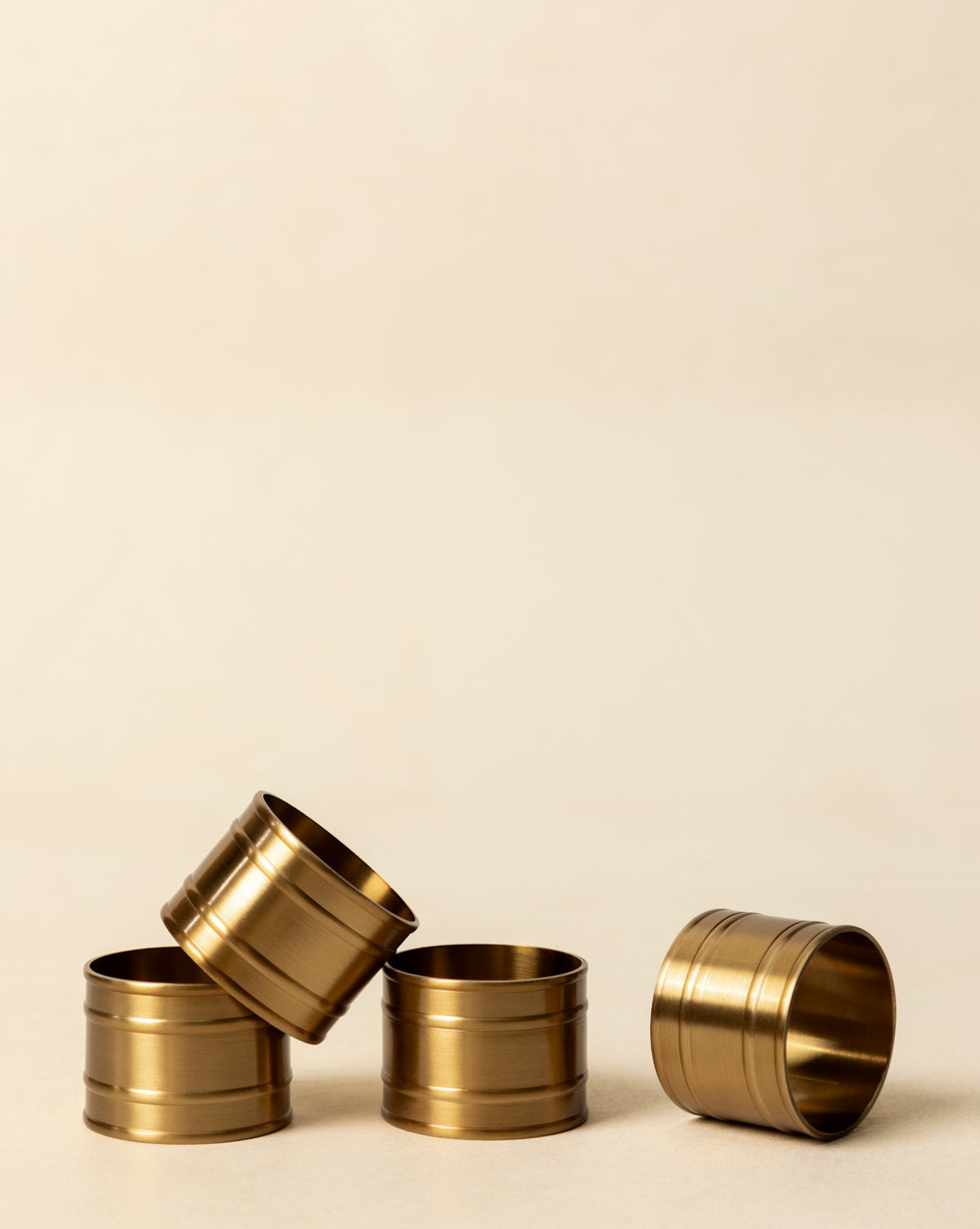The Argent Napkin Rings (Set of 4) are arranged on a soft beige surface—three upright and clustered, one leaning diagonally—creating a warm, inviting accent for your holiday table, by Vendixs