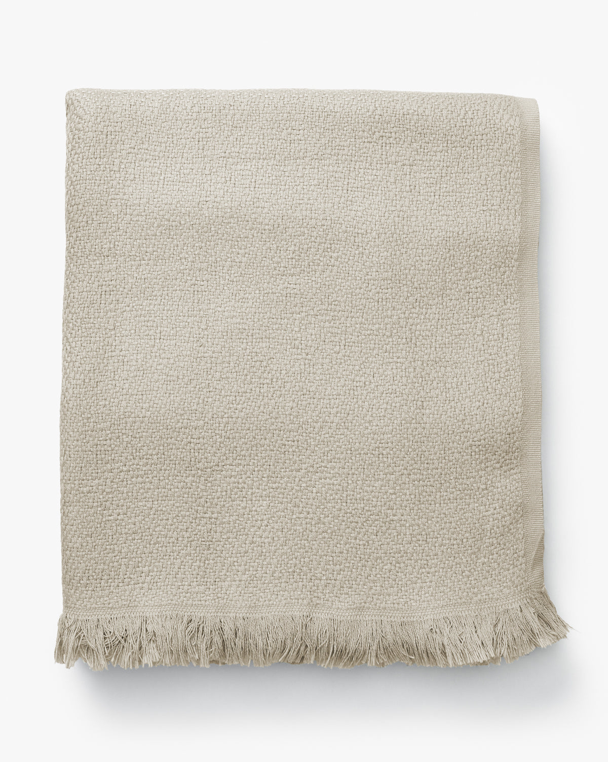 The Ariella Throw by J Call Designs LLC dba Sew Miami LLC is a folded beige cotton throw with a textured finish and short fringe, shown on a white background—ideal for adding warmth to any neutral decor. Vendixs