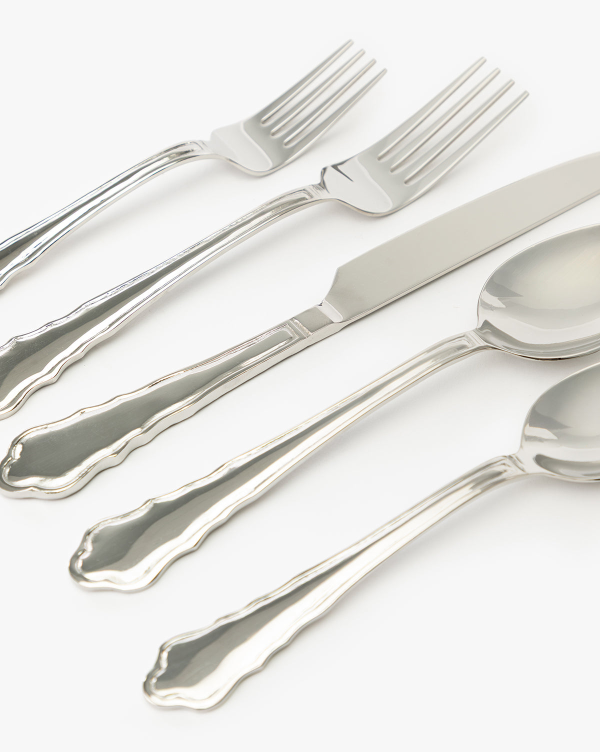 The Artois Flatware (Set of 5) features vintage-inspired pieces—two forks, a knife, and two spoons—each with elegant scalloped edge handles, artfully arranged diagonally on a white background by Vendixs
