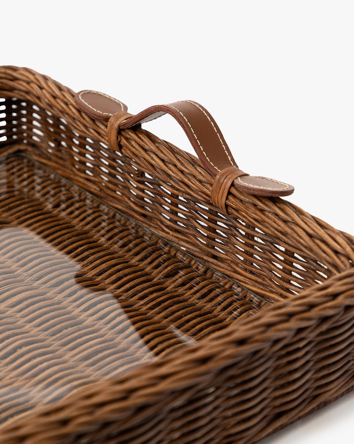 A close-up of the Ashcroft Wicker Tray—a rectangular woven basket with a brown leather handle on one side—set against a plain white background, highlighting the detailed wicker texture, by McGee & Co.