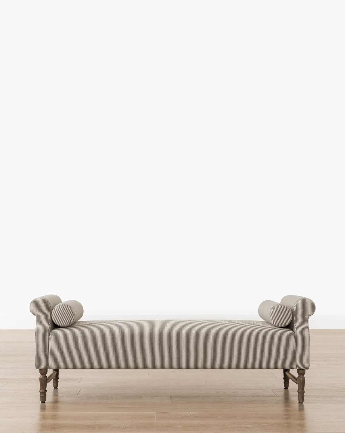 The Asher Bench offers gray upholstered seating with striped linen bolster pillows at each end, supported by wooden legs, and is shown on a wooden floor against a plain white background, by Vendixs