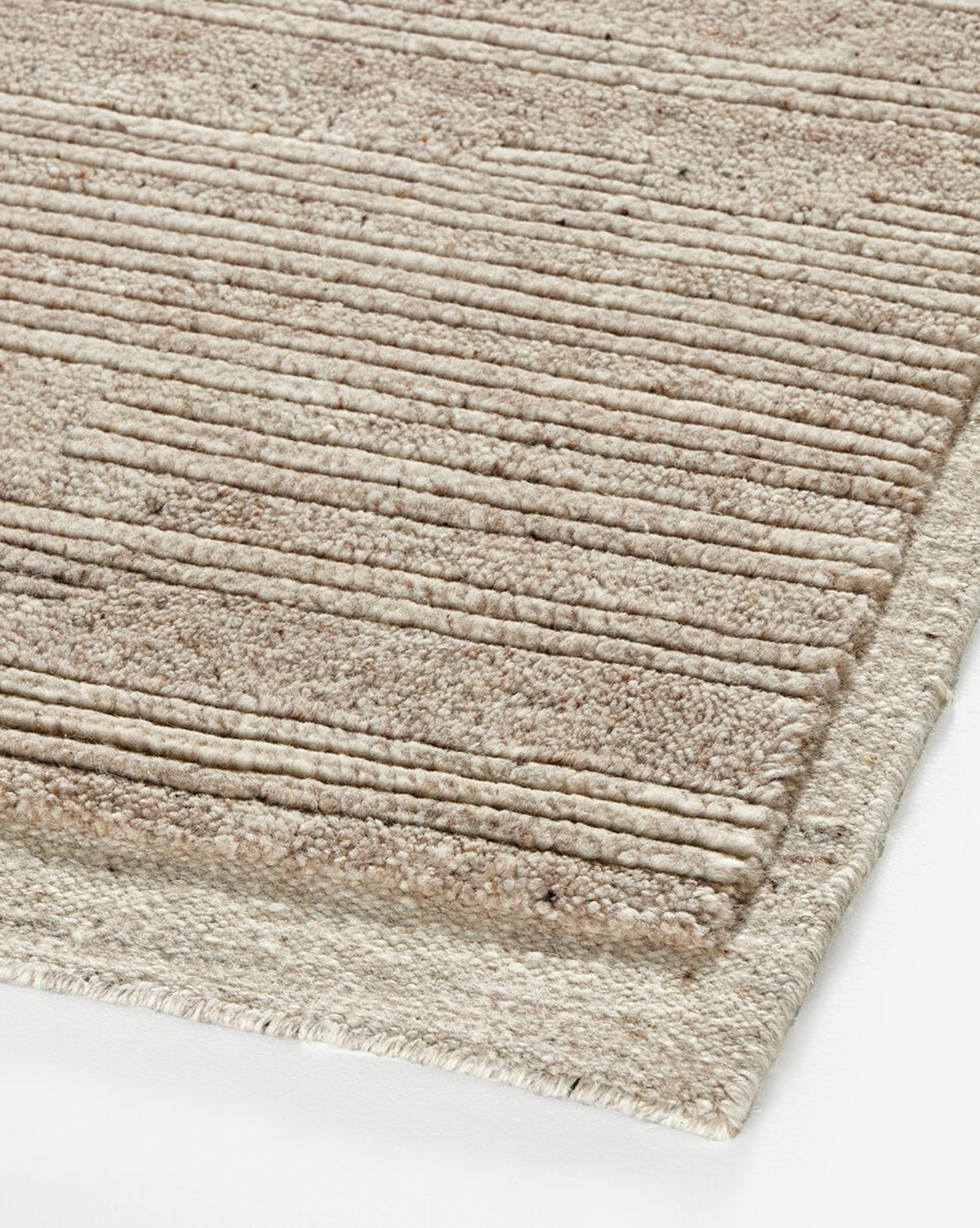 A close-up of the Ashwin Hand-Knotted Wool Rug shows its beige, textured wool surface with horizontal raised stripes, neatly finished edges, and a neutral palette resting on a white background, by Vendixs