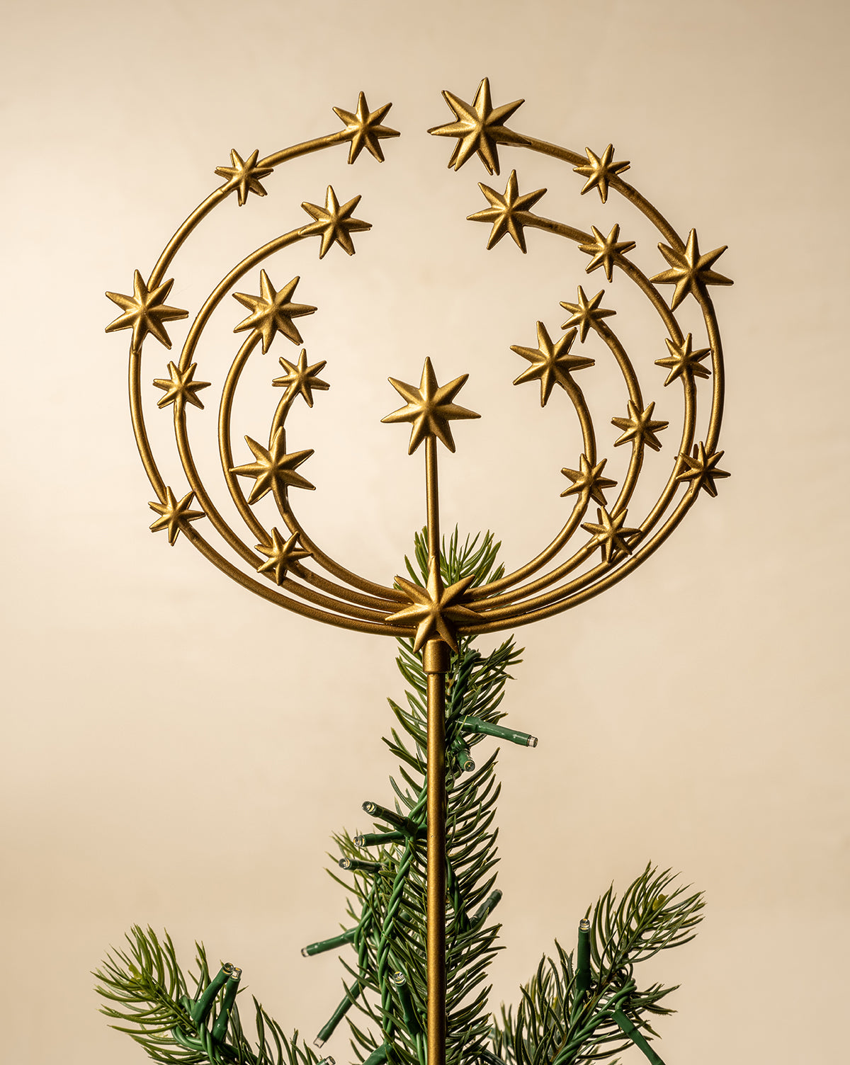 The Astra Brass Tree Topper features a gold design with radiating rings and stars in an antique brass finish, elegantly crowning an artificial Christmas tree against a neutral background for sophisticated holiday decor, by Vendixs
