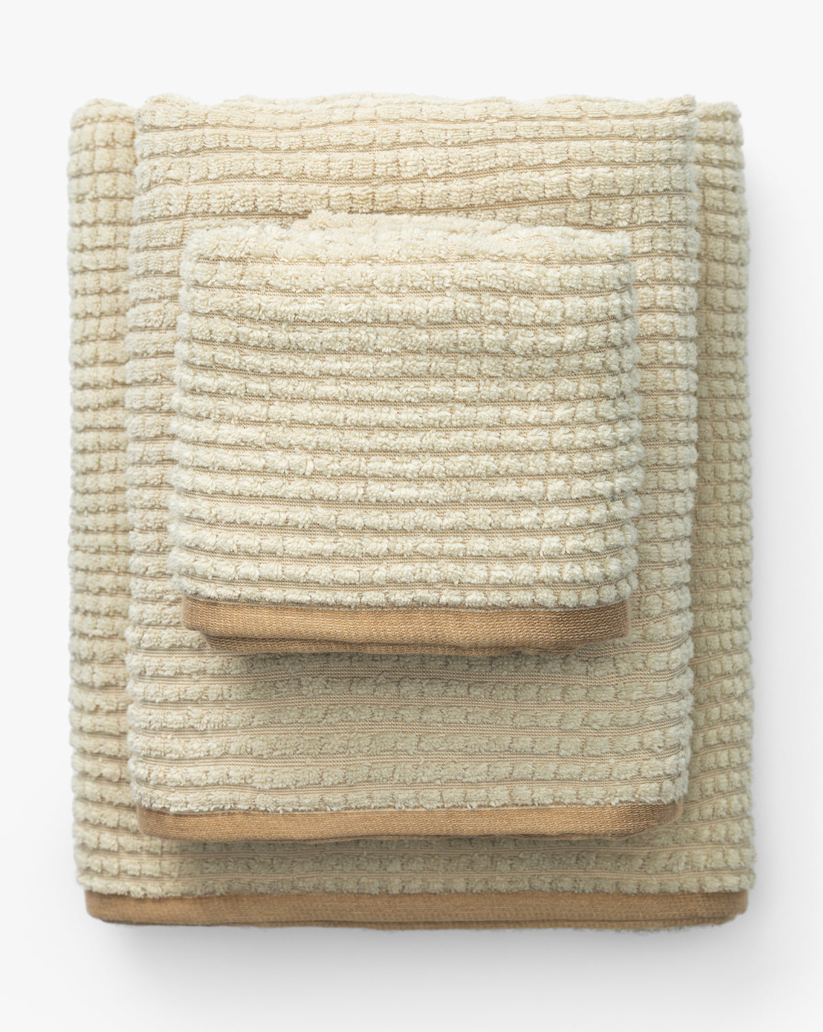 A neatly stacked set of three beige organic cotton towels from the Atrani Organic Bath Collection, featuring a textured waffle weave, arranged largest to smallest on a white background, by Vendixs