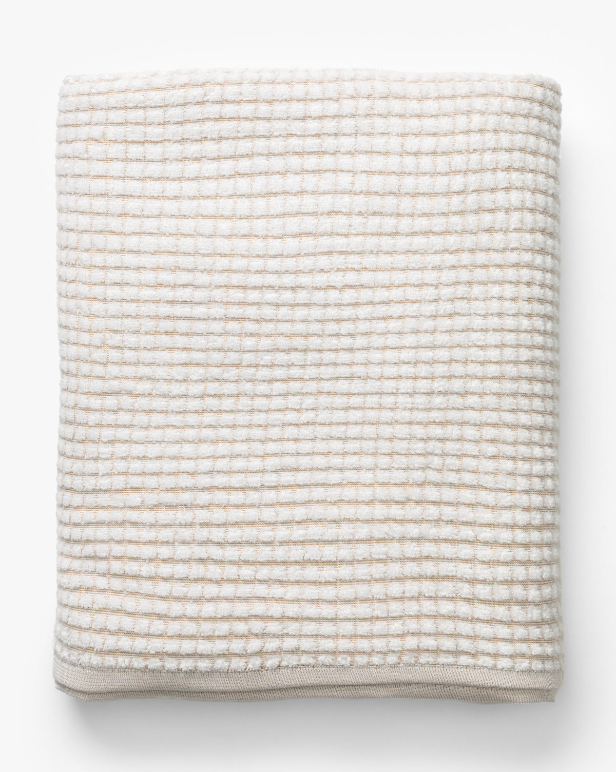 A neatly folded towel from the Atrani Tan Organic Bath Collection, featuring a beige and white checkered waffle weave in soft, textured organic cotton, displayed on a white background by Vendixs