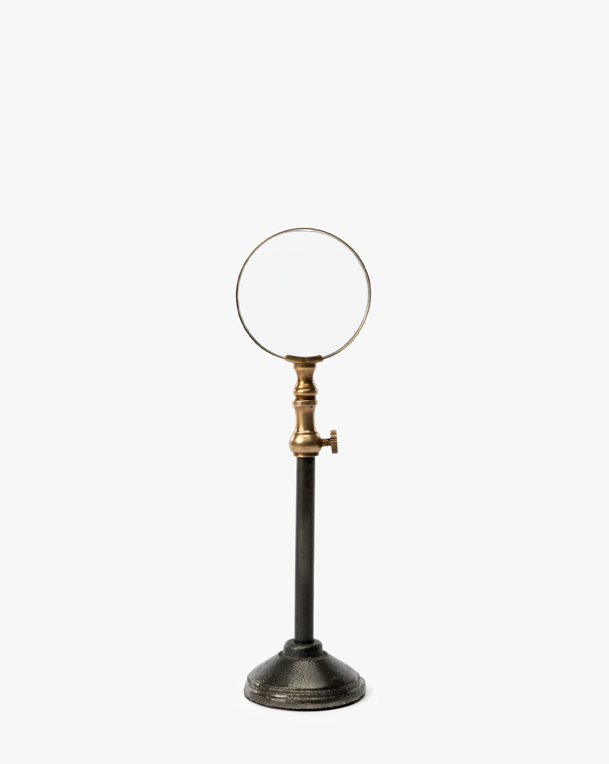 The Barnabas Standing Object features a vintage round lens, burnished brass holder with adjustable knob, and tall black metal stand with a heavy circular base—an elegant home decor piece displayed against a white background, by Vendixs