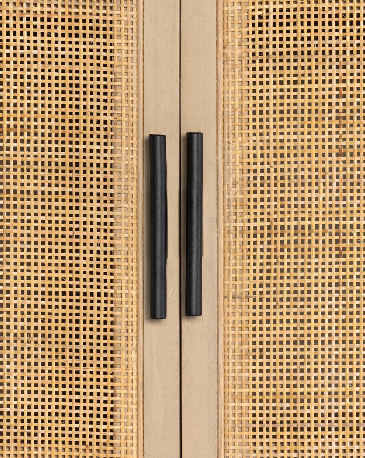 Close-up of two black handles on the Barney Cabinet, a black-washed wood piece with light cane doors. The vertical handles are centered, accentuating the cabinets modern design and woven rattan panel detail, by Vendixs