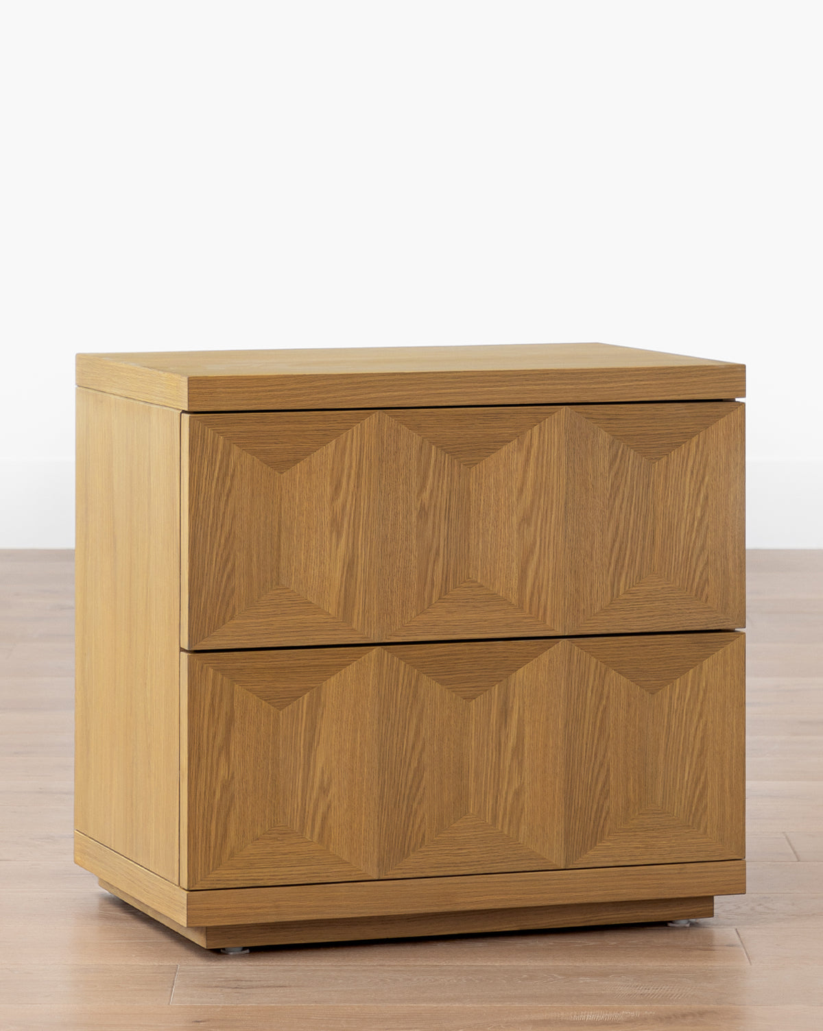 The Beacon Nightstand is a modern piece crafted from white oak, featuring two drawers with a geometric textured front, by McGee & Co. It sits on a flat base, perfect for stylish bedroom storage.