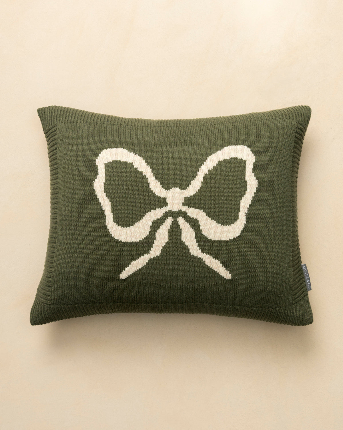 The Bella Pillow Cover is rectangular, dark green, and features a large cream bow in the center. Its cozy knit texture makes it perfect for holiday layering, by Vendixs