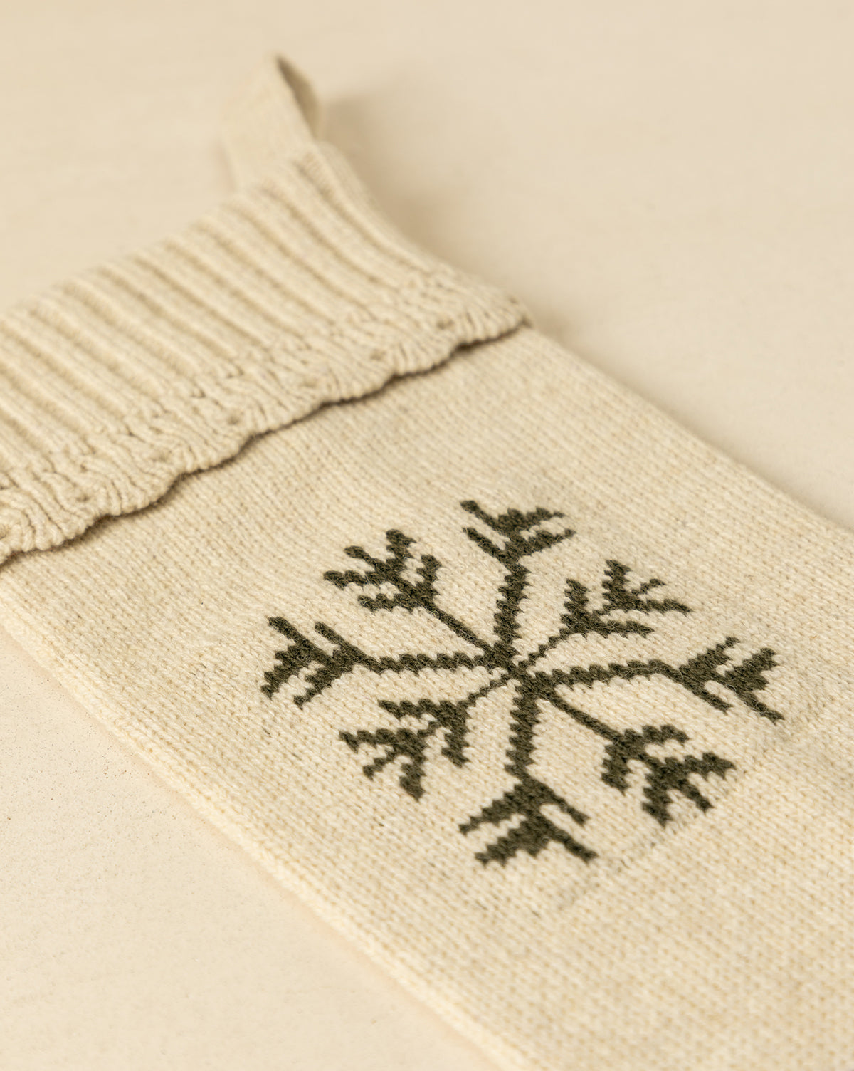 The Bella Scalloped Stocking with Snowflake, in cream knit with a dark green snowflake design, is displayed on a beige surface—an ideal festive addition to your holiday mantel decor, by Vendixs