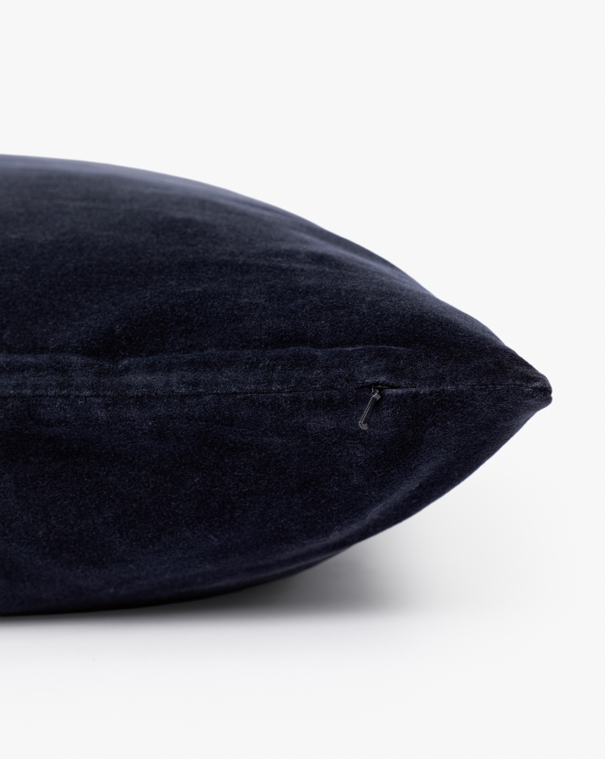 A close-up of the Bellevue Velvet Pillow Cover in dark navy blue shows its side zipper, set against a plain white background—ideal as a stylish decorative accent for your sofa, by Vendixs