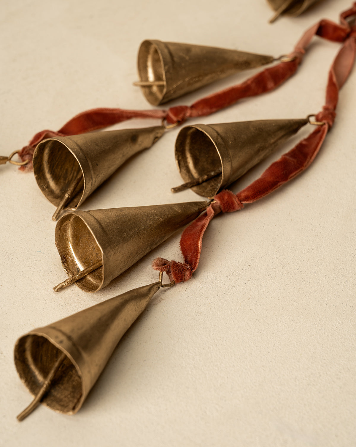 A close-up of the Bells on Velvet Ribbon Door Hanger, featuring several cone-shaped gold bells attached to velvet ribbon and displayed on a light textured surface for a charming festive accent, by Vendixs