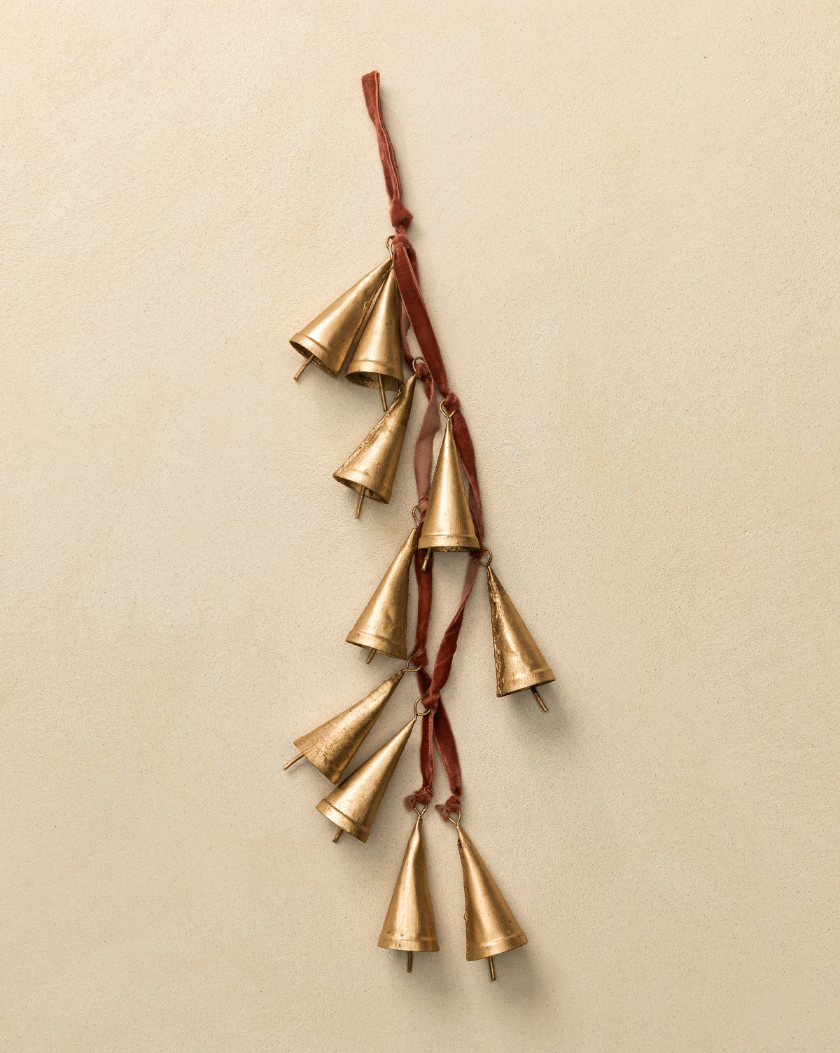 The Bells on Velvet Ribbon Door Hanger features nine small gold cone-shaped metal bells suspended from rich velvet, creating a festive accent against any beige wall, by Vendixs