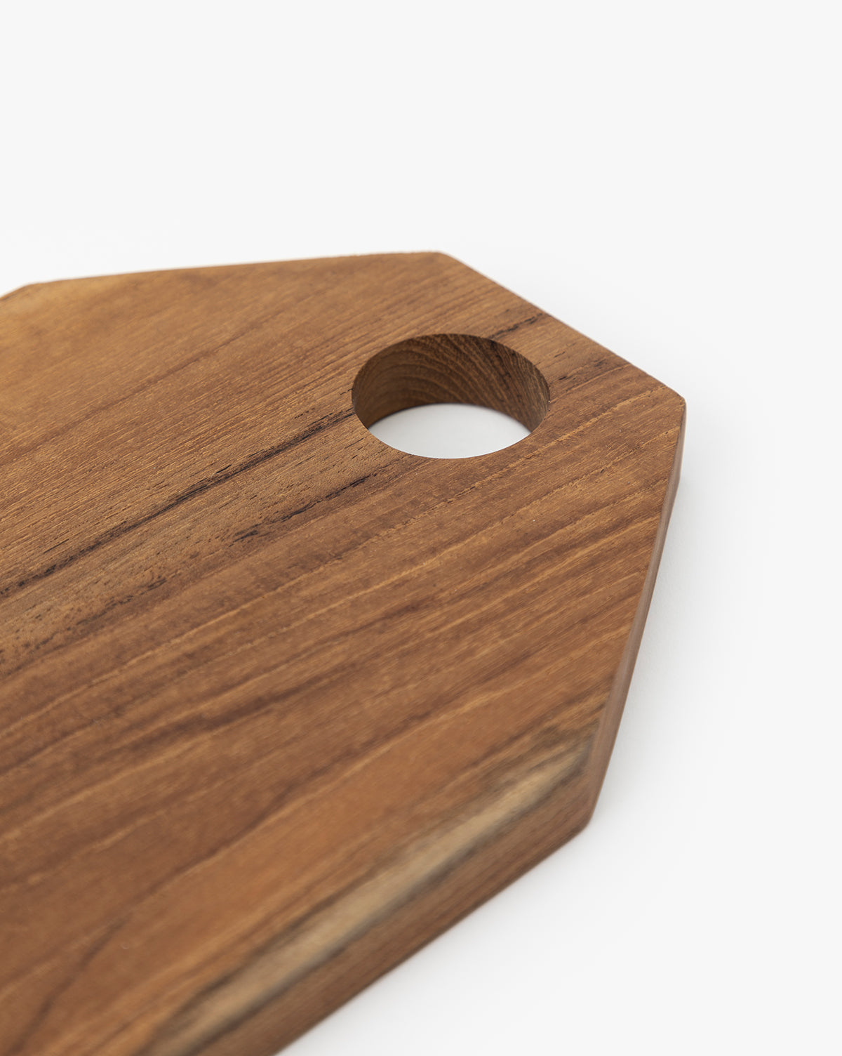 A close-up of the Bevelled Edge Cutting Board, pentagon-shaped with a round hole near one corner, crafted from teak root and set against a white background—a must-have for any home chef, by Vendixs