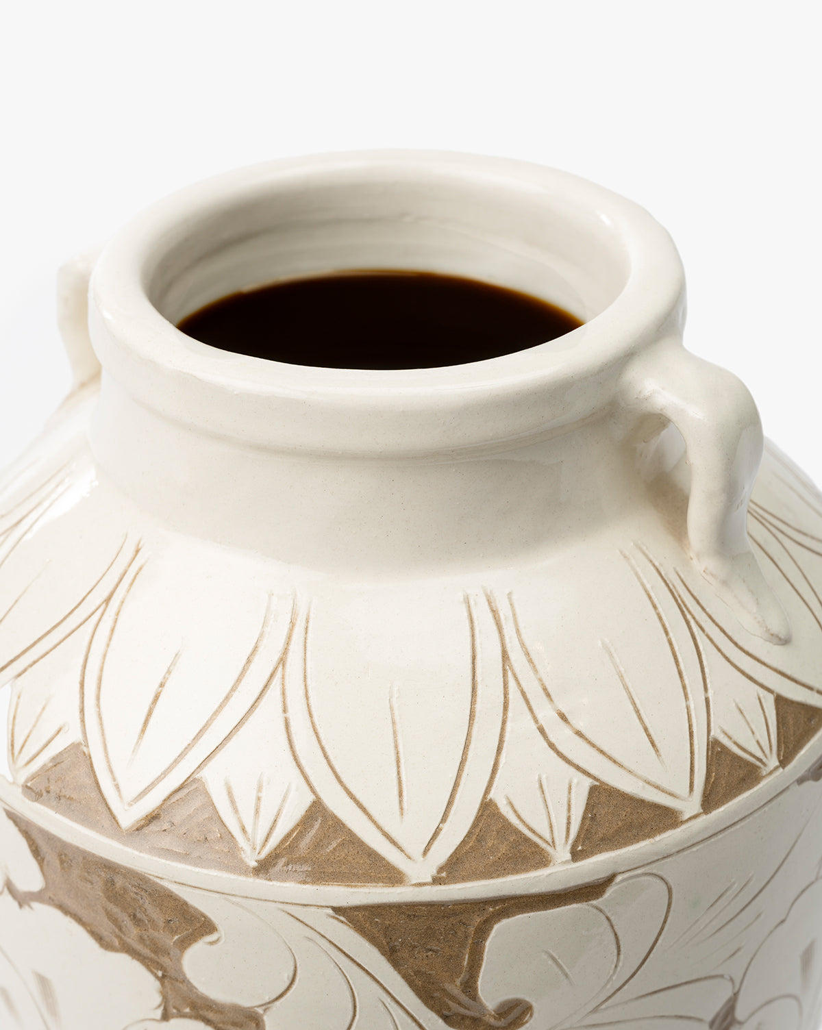 A close-up of the cream-colored Blaise Vase, handmade with an open mouth, two small side handles, and an etched leaf pattern—partially filled with a dark liquid for an elegant touch to your home decor, by Vendixs
