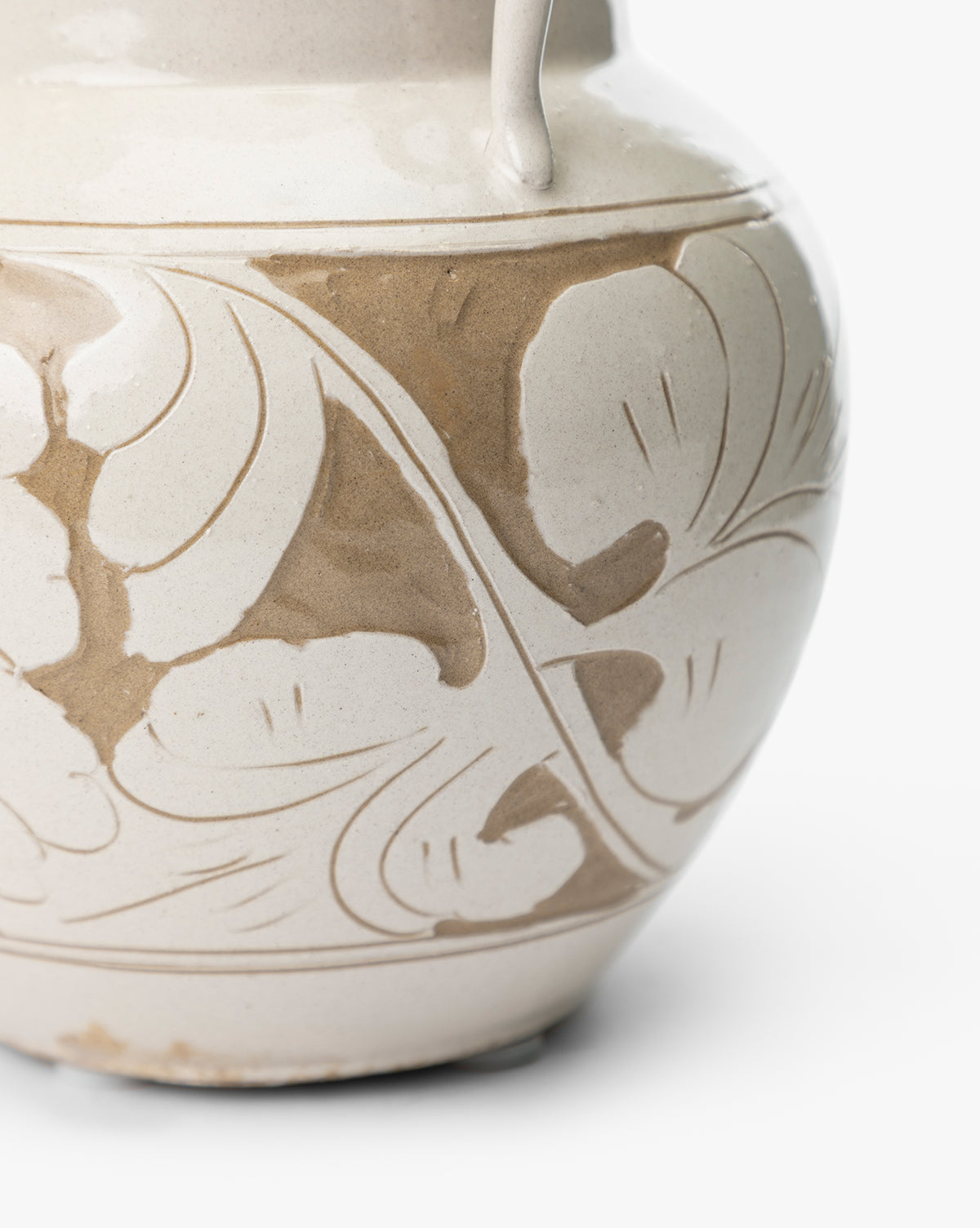 A close-up of the Blaise Vase, handmade with a light beige glaze and an abstract floral pattern in darker tan curving around its rounded surface, making it a unique home decor piece, by Vendixs