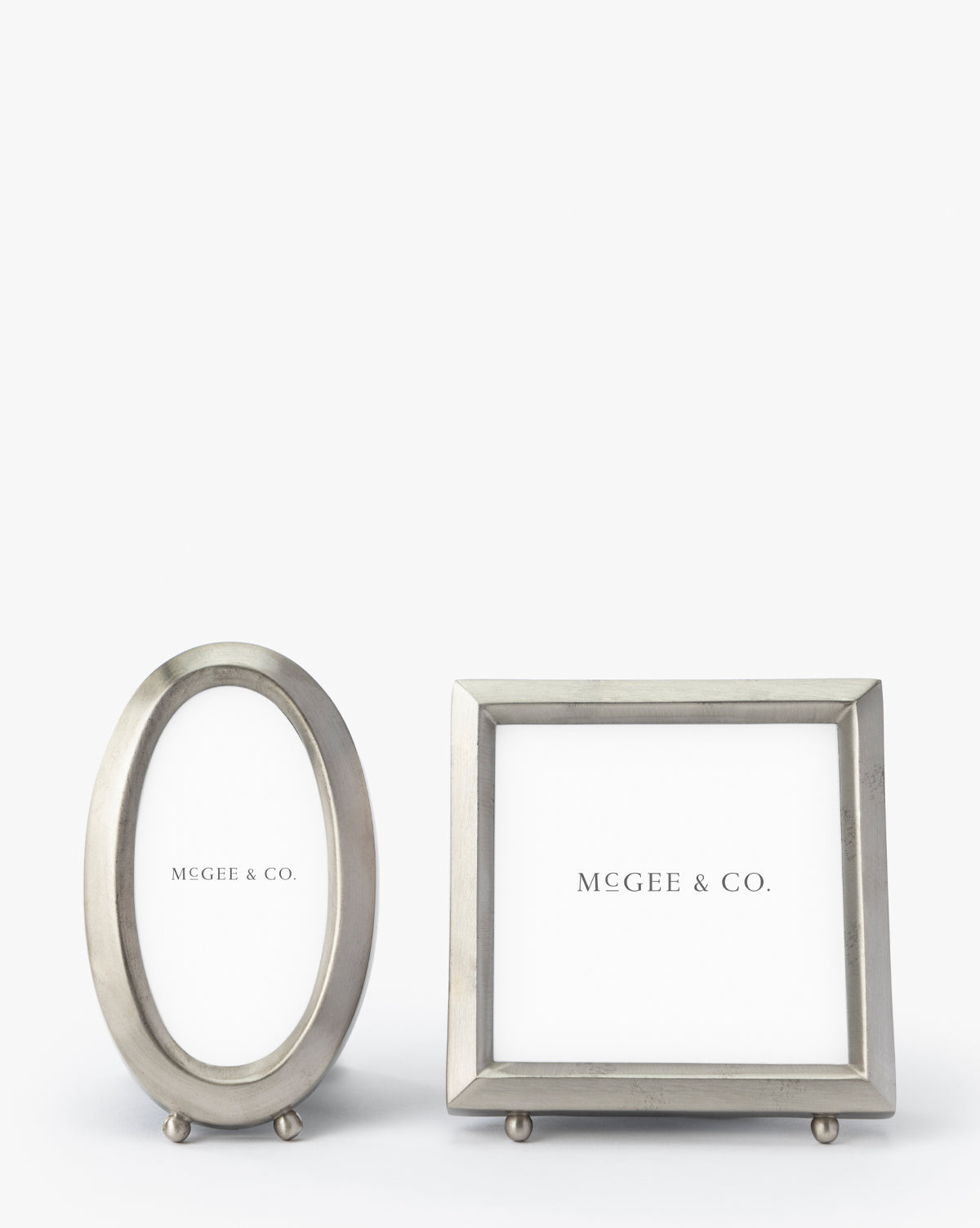 The Blanche Pewter Picture Frame, shown in both oval and rectangular shapes with small round feet, features a sophisticated design and MGEE & CO. placeholder text against a white background.