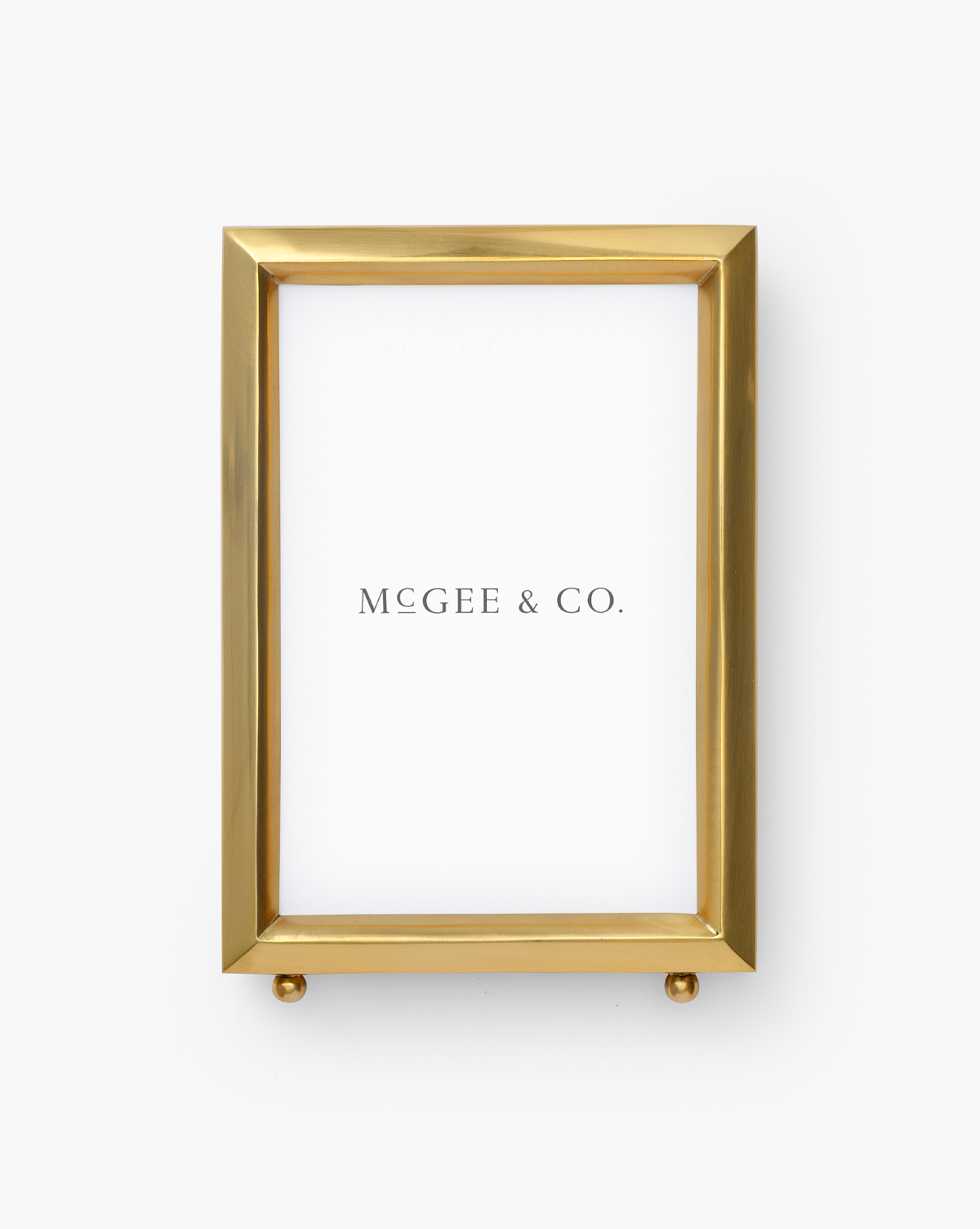 A gold Blanche Picture Frame featuring a polished brass finish and white background, with “McGee & Co.” elegantly in black lettering, by Vendixs