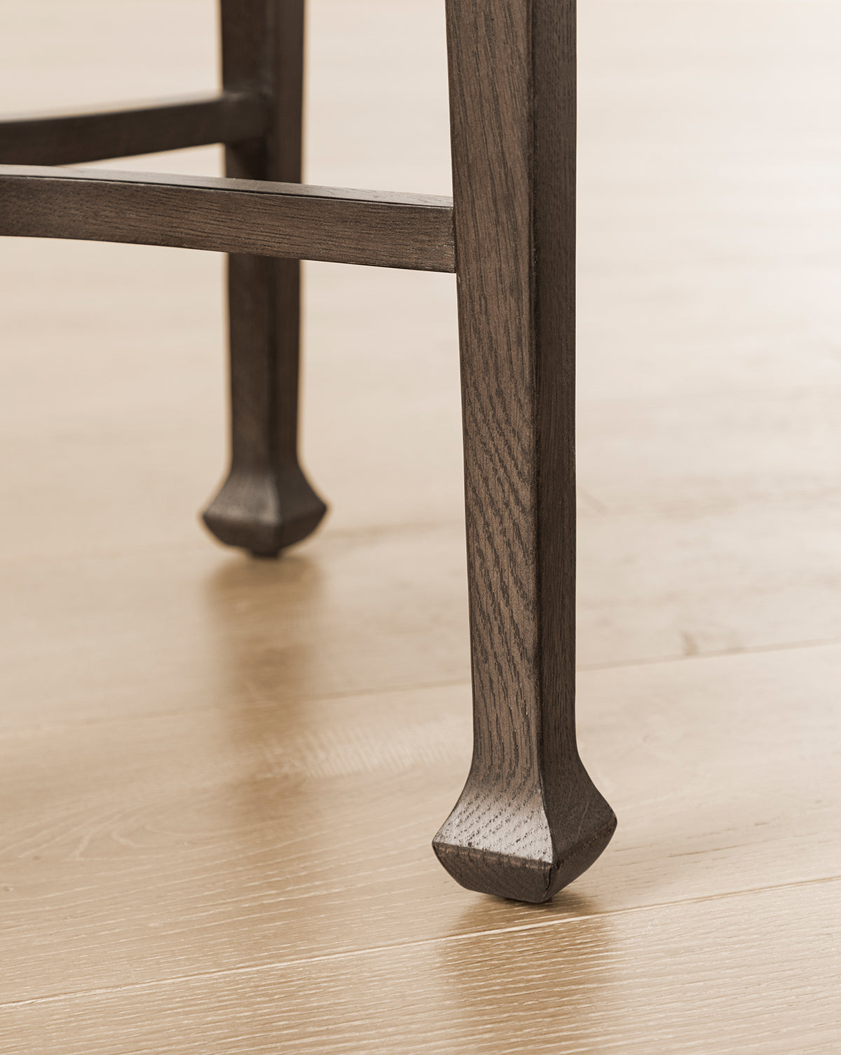 Close-up of the Bradshaw Side Table legs on a light wood floor, showcasing antique-inspired flared feet and a textured satin walnut oak grain, by Vendixs