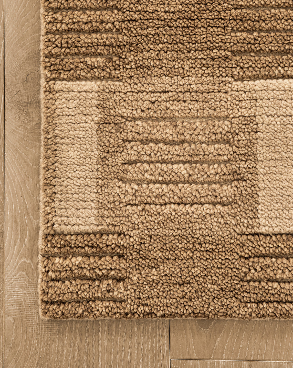 A close-up of the Brenner Hand-Knotted Wool Rug, showcasing its textured beige and brown geometric pattern with raised rectangular and linear designs, placed on a light wood floor for added depth, by Vendixs