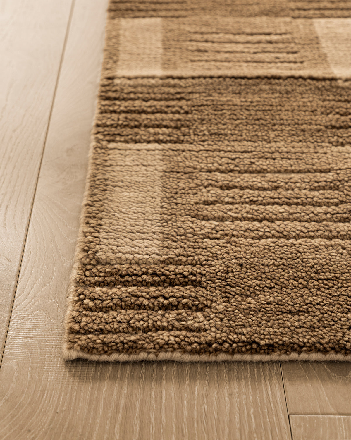 Close-up of the corner of the Brenner Hand-Knotted Wool Rug, featuring a beige and brown geometric pattern, placed on light-colored wooden flooring by Vendixs