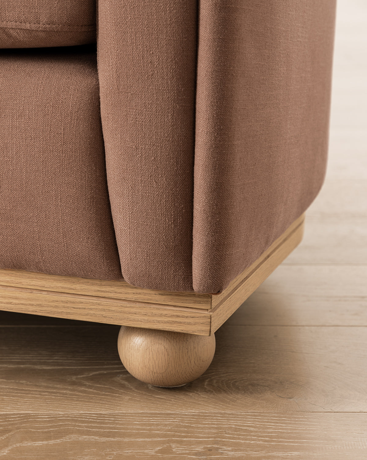 Close-up of the Bunnell Lounge Chair (Ready to Ship) corner, highlighting its textured dusty rose upholstery, light wooden base, and rounded leg—a modern traditional chair on light wood flooring, by Vendixs