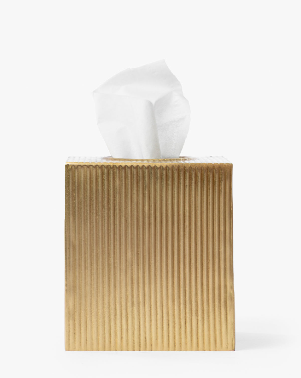 The Calvert Brass Tissue Box Cover, featuring a gold fluted design and white tissue emerging from the top, creates an elegant accent against a plain white background, by Vendixs