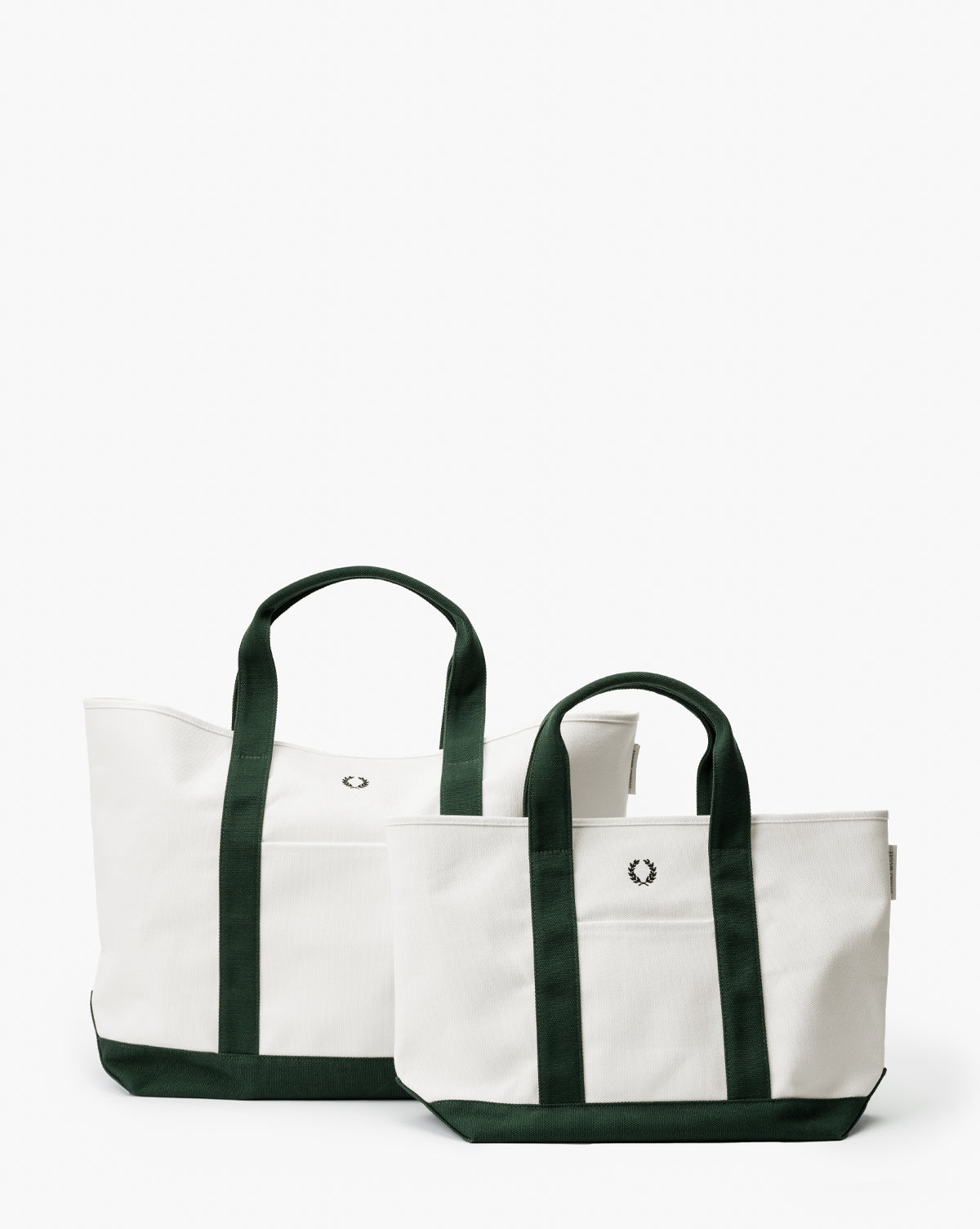 Two white Canvas Laurel Totes with dark green handles and bottoms, each featuring a small embroidered laurel wreath. The larger tote is placed behind the smaller one, creating a stylish, layered look, by Vendixs