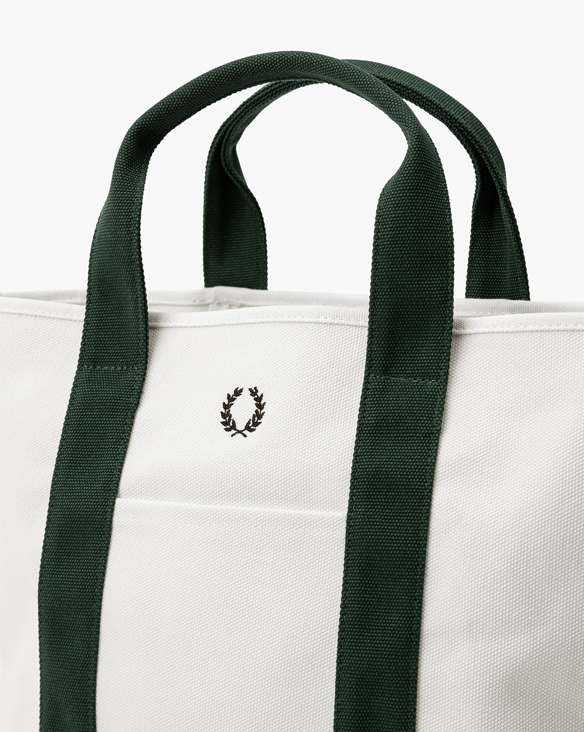 A close-up of the Canvas Laurel Tote highlights its white canvas, dark green handles, and a small black laurel wreath logo embroidered on the front pocket—making it perfect for everyday use, by Vendixs