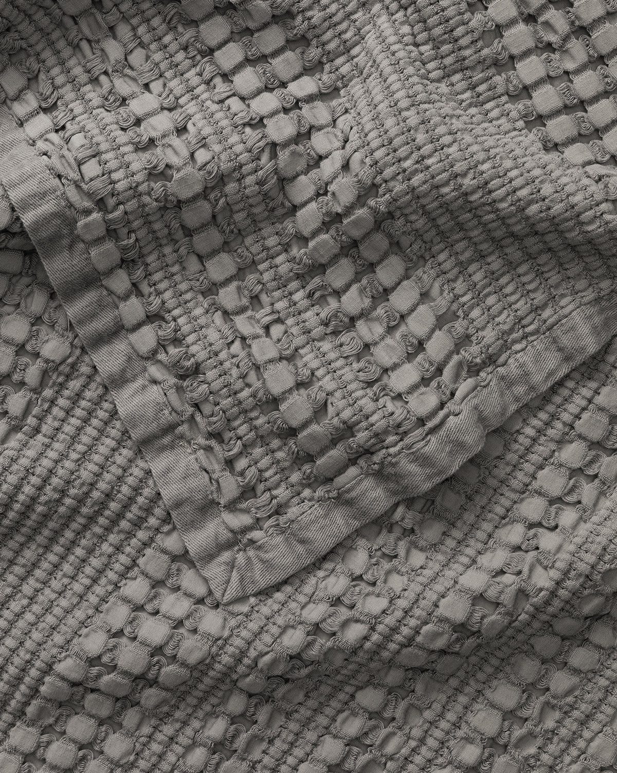A close-up of the Penedo Carnel Gray Waffle Blanket shows its solid gray, textured woven fabric with raised rectangular and circular patterns for a three-dimensional look. Vendixs