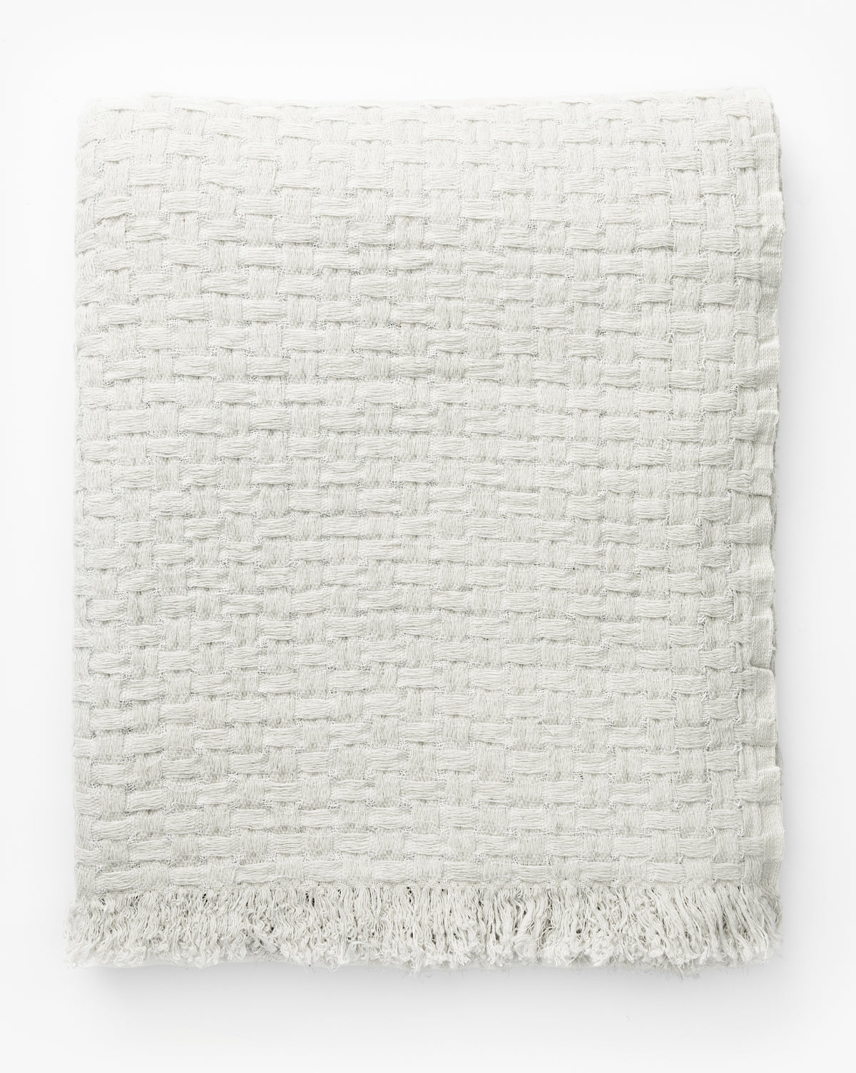The Caroline Kids Blanket by Indigo Craft is an off-white, textured woven blanket with fringe at the bottom edge, shown folded on a white background by Vendixs