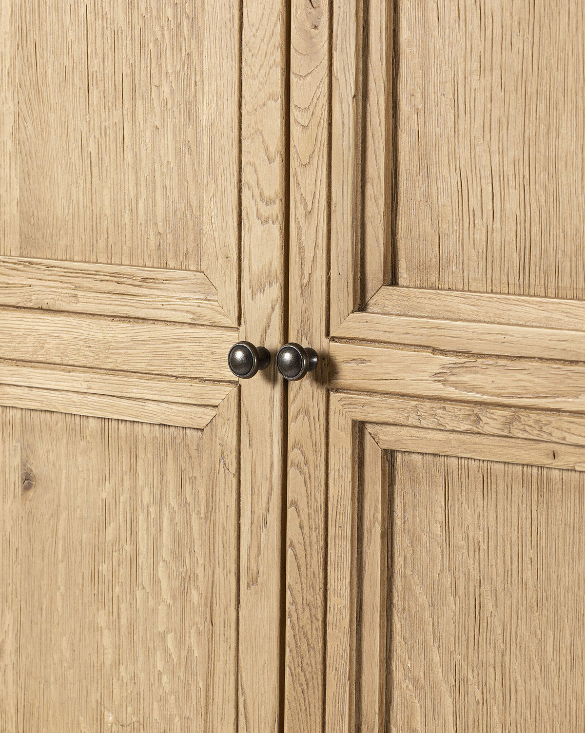 Close-up of Carrington Cabinet doors in worn oak with a light, natural grain and two central round, bronze-finished knobs, by Vendixs