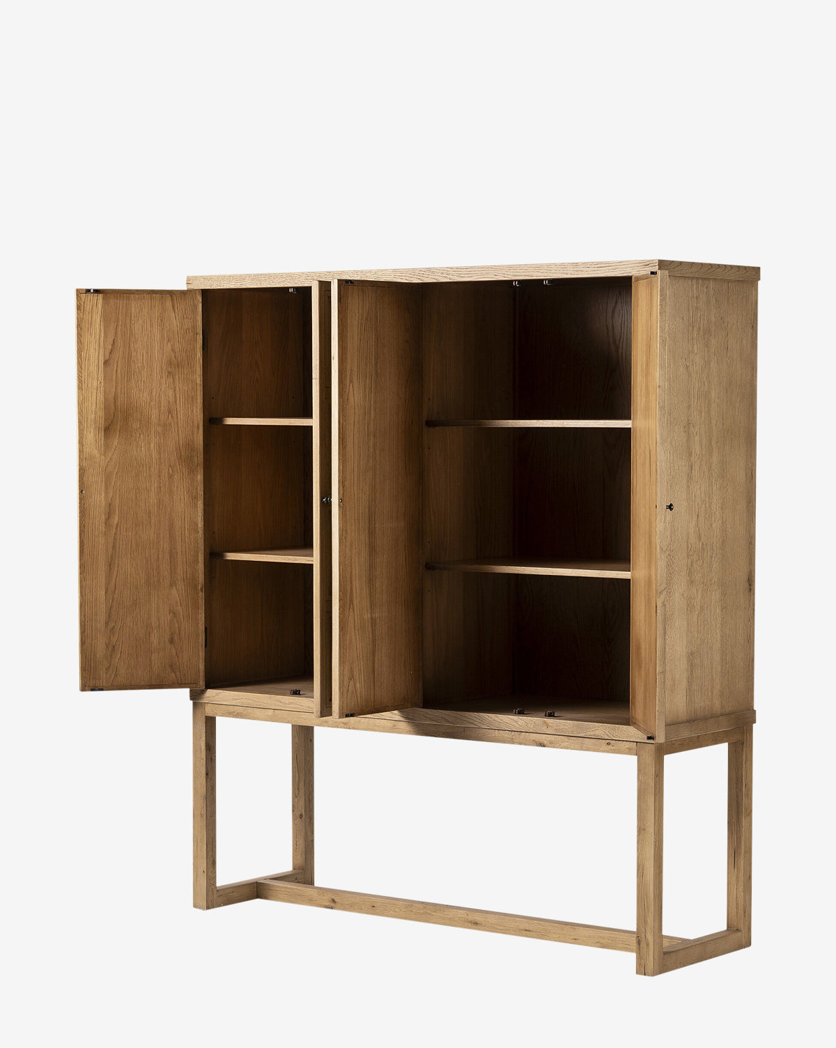 The Carrington Cabinet, made from worn oak with bronze-finished hardware, stands on a simple rectangular frame. One of its two doors is open, showing three interior shelves, all set against a plain white background by McGee & Co.