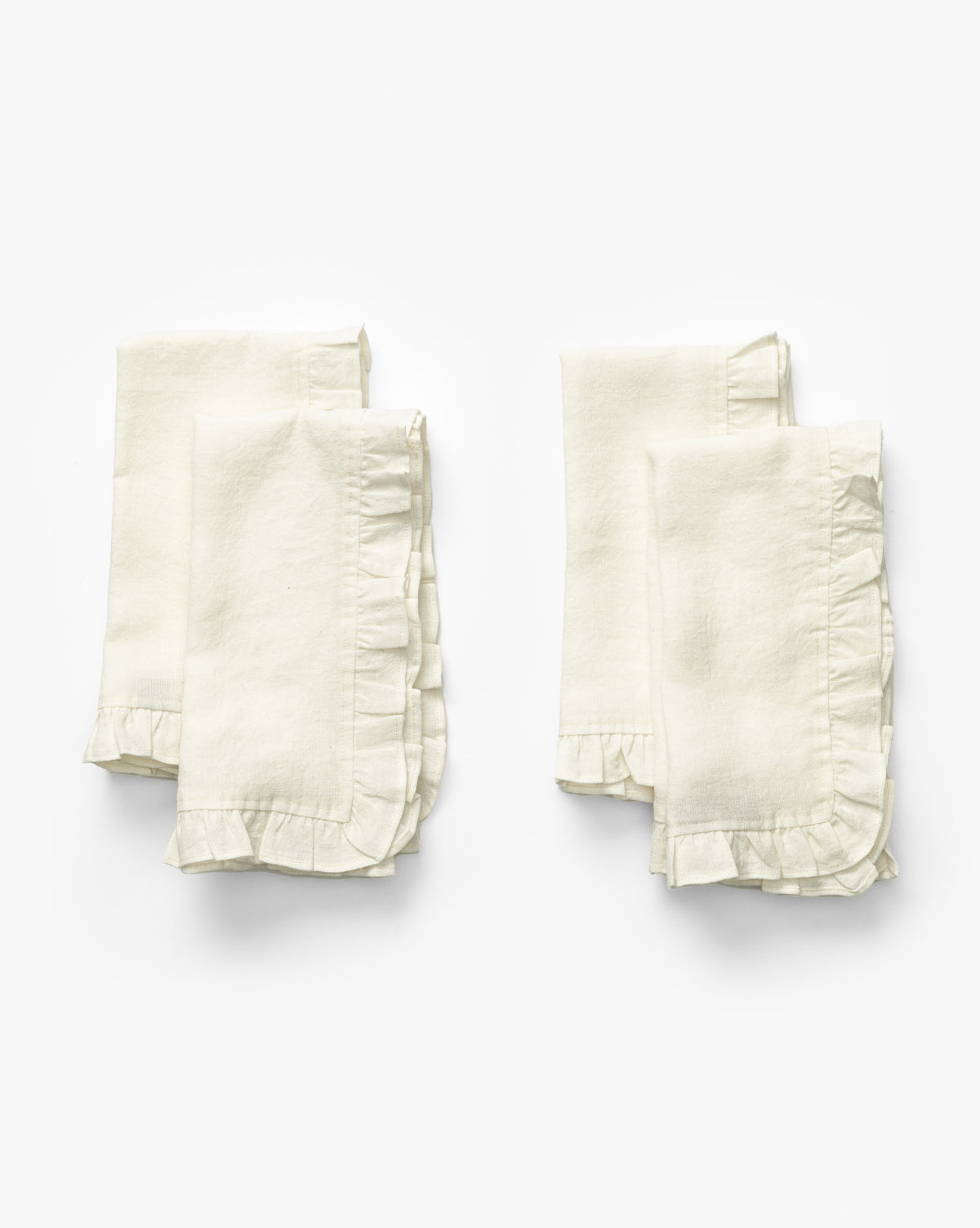 A set of four Catania Linen Napkins, off-white with delicate ruffled edges, is folded and arranged in two pairs on a plain white background by Vendixs