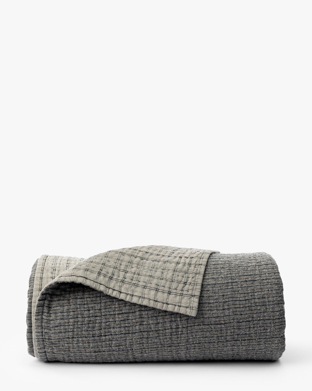 The Cecily Kids Quilt by Renuka Inc. features a neatly folded, textured gray design with a lighter gray grid-patterned underside, displayed on a white background. Vendixs