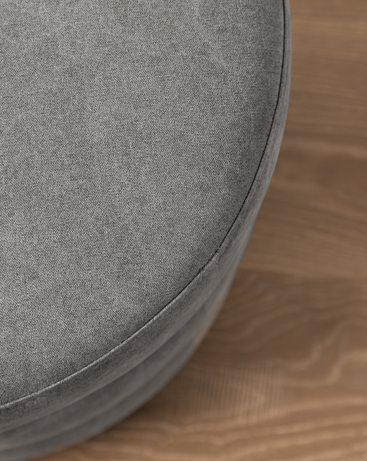 A close-up of the Channel Ottoman features its round, quilted gray design on a light brown wooden floor, adding a touch of midcentury style, by Vendixs