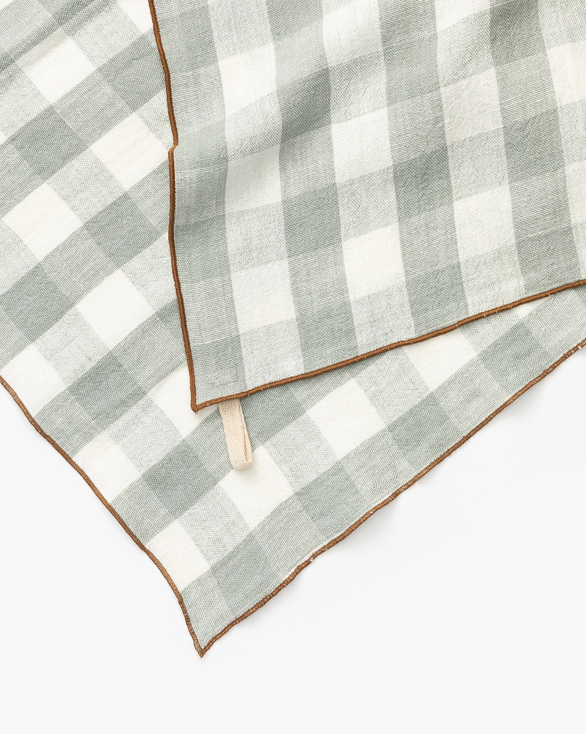 A close-up of two Charlie Check Tea Towels, featuring gray and white checkered linen with brown stitched edges, slightly overlapping on a white background—ideal for stylish table settings, by Vendixs