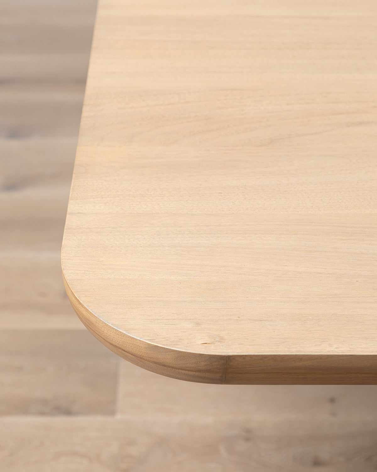 A close-up of the Cheswick Dining Tables corner highlights its modern walnut finish and rounded edges, set against a matching wooden floor, by Vendixs