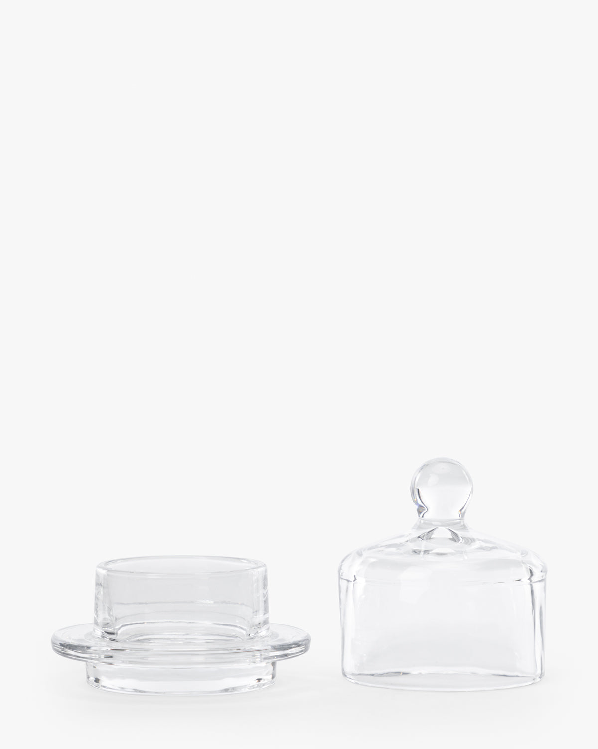 The Christian Glass Condiment Dish features a clear round base and a matching domed lid with a small knob handle, shown side by side on a white background—ideal for serving condiments or butter in style, by Vendixs