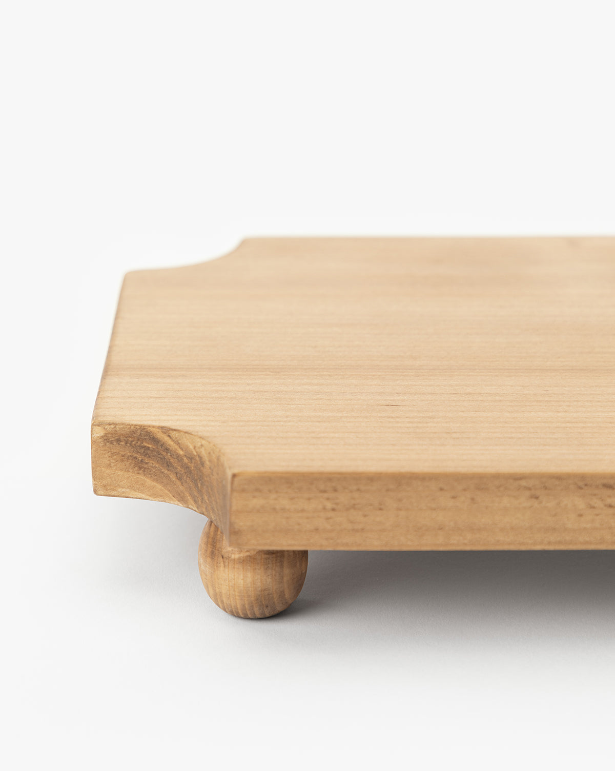 A close-up of the Cillian Pedestal Board, a rectangular pine wood board with rounded corners and small round legs, displayed on a white surface, by Vendixs