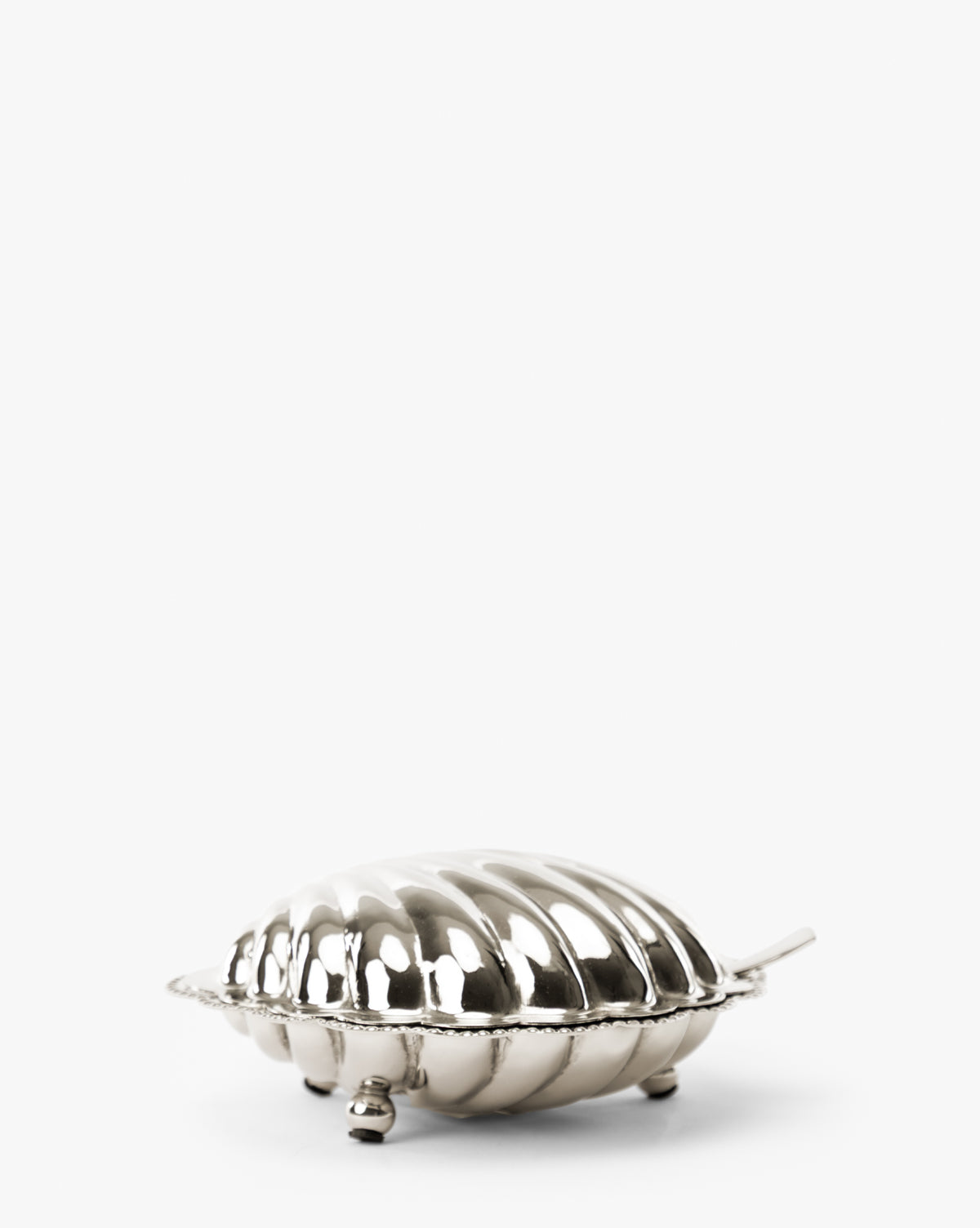 A small, shiny Clam Shell Serving Dish with Spoon, shaped like a shell with a ridged lid, three small feet, and a short handle, displayed on a plain white background, by Vendixs