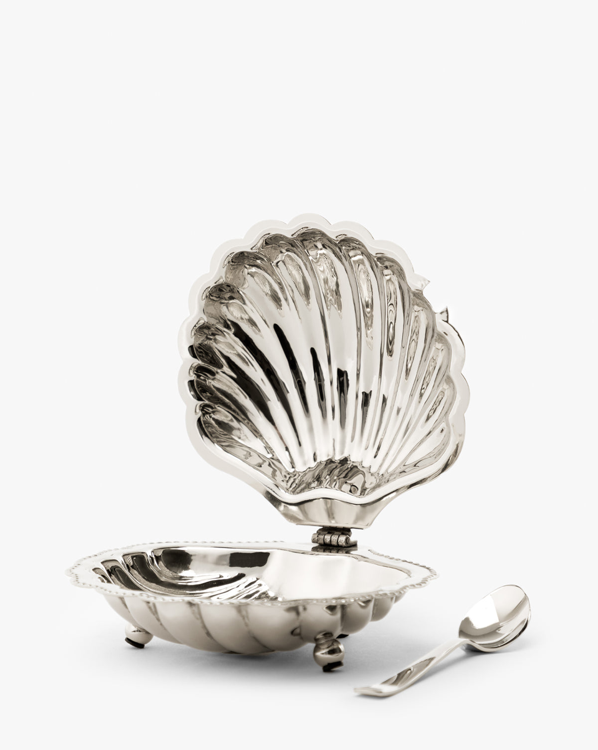 The Clam Shell Serving Dish with Spoon is open to show its reflective interior. A matching small silver spoon sits beside this elegant, hinged-lid serving dish, perfect for nautical-themed decor or entertaining by Vendixs