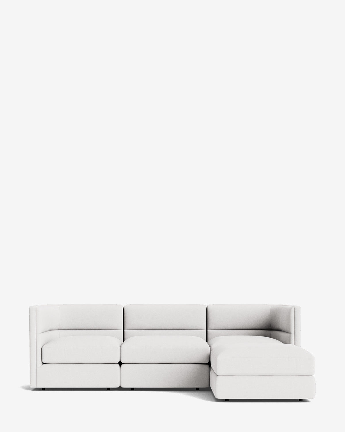 The Claremont Modular Sofa with Ottoman 99 is a modern white sofa featuring three seats, a right-side chaise lounge, and a sleek channeled back, set against a plain white background, by Vendixs